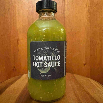 Bottle of locally grown and bottled tomatillo hot sauce on a wooden surface.